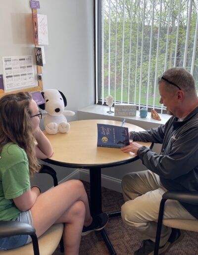 Person sitting at table with author smiling while getting their copy of Lucy’s Way signed
