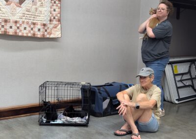Elwood Library Adult Services Manager Wendy Rivera, standing, holds Diego, while Elwood Animal Shelter volunteer Vicki Savage sits with Thug and Tug during Mark's reading on August 8, 2026.